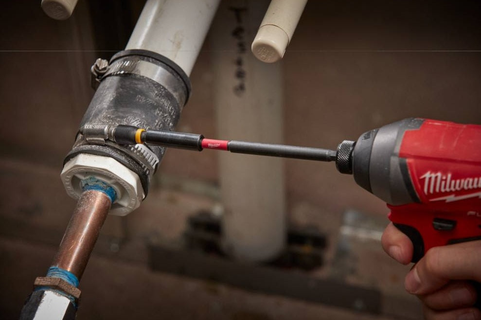 Power drill with magnetic bit holder tightening pipe fitting in plumbing setup, part of woodworking tool accessories.