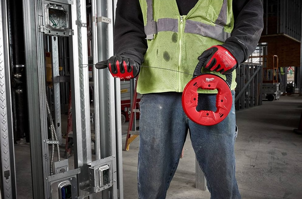 Worker wearing safety vest holding red steel fish tape used for electrical wiring in construction and home improvement tasks