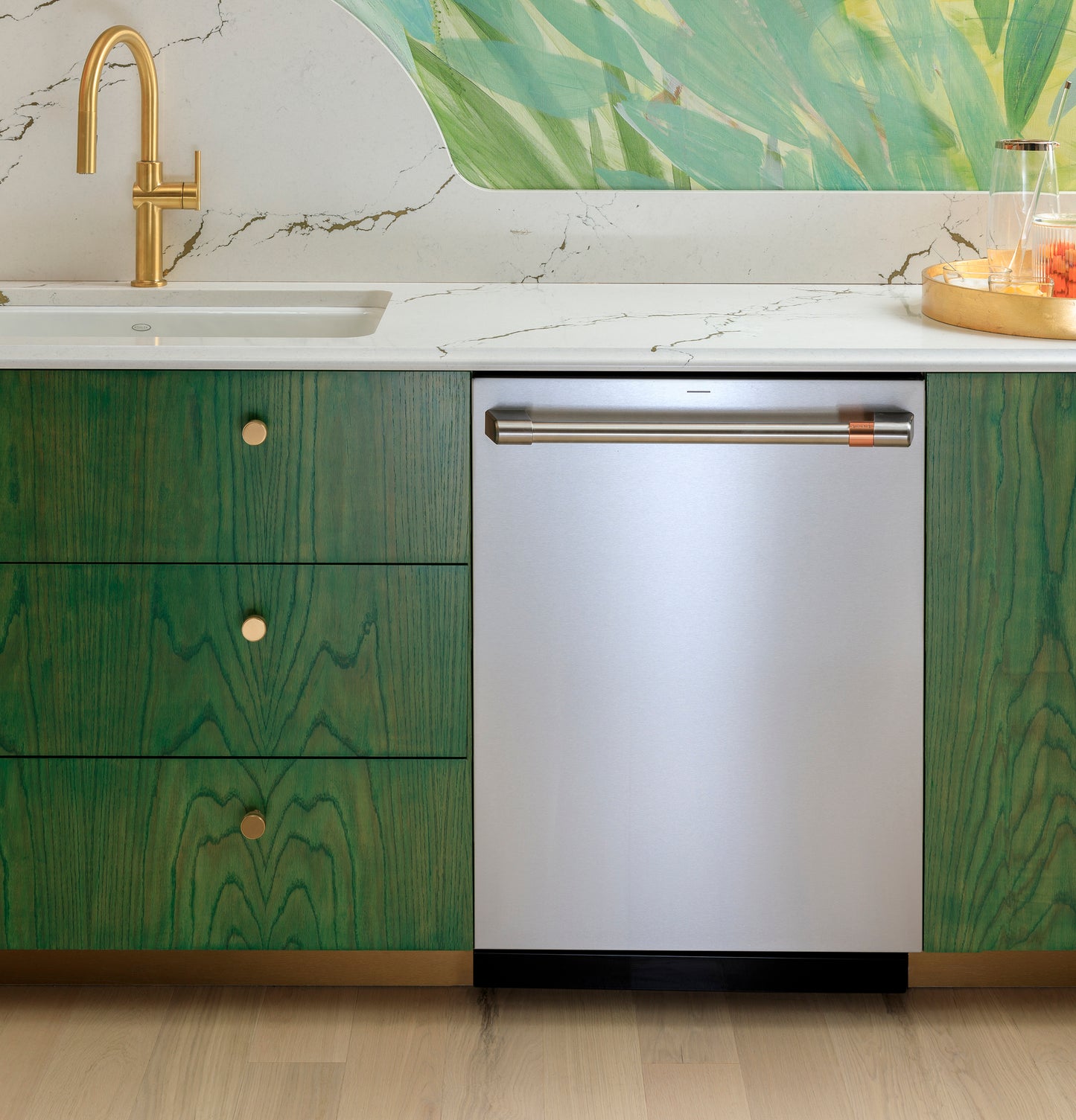 Built-in stainless steel dishwasher with copper-accented handle integrated into green cabinetry in modern kitchen setting