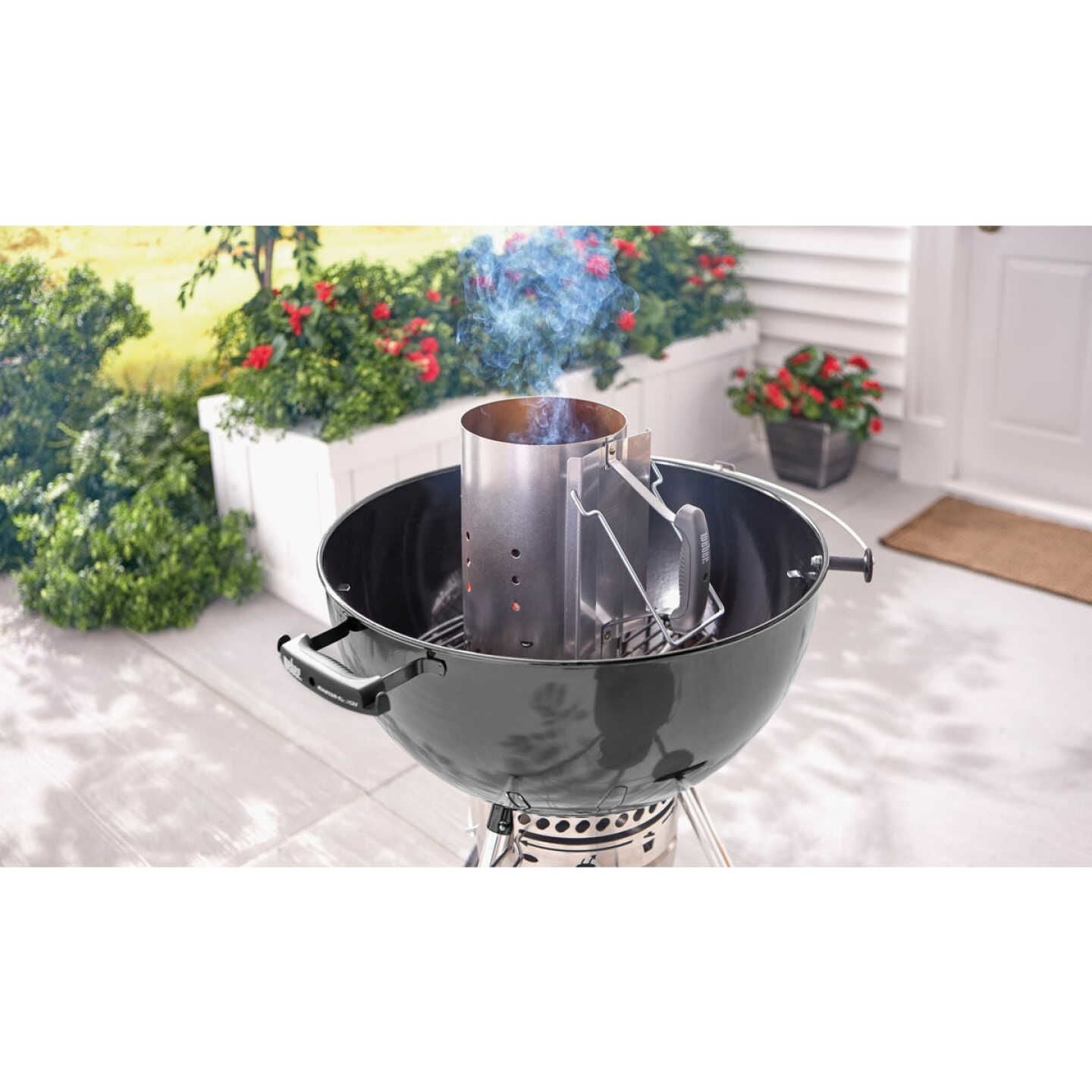 Steel chimney charcoal starter with handle heating briquettes inside kettle grill on outdoor patio setting