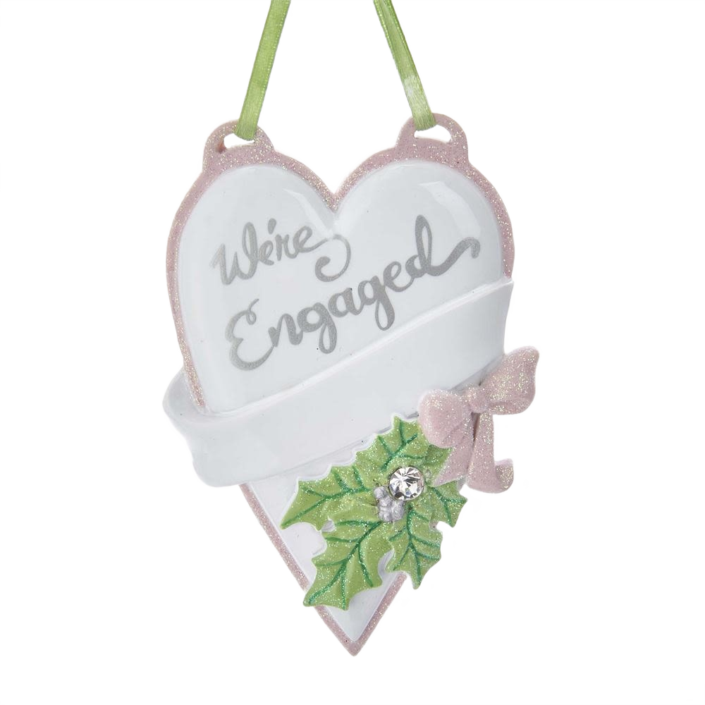 Heart-shaped ornament with "We're Engaged" text, decorated with holly leaves and pink bow for personal celebrations