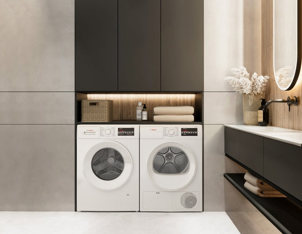 Modern laundry space with white front-load washer and compact Bosch condensation dryer set into sleek black cabinetry under warm lighting