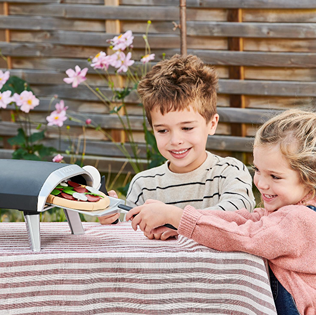 Children playing with a compact pizza oven toy cooking a pretend pizza during outdoor imaginative playtime