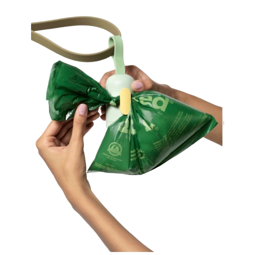 Light green Earth Rated dog waste dispenser with beige strap holding green waste bag in hands for outdoor use