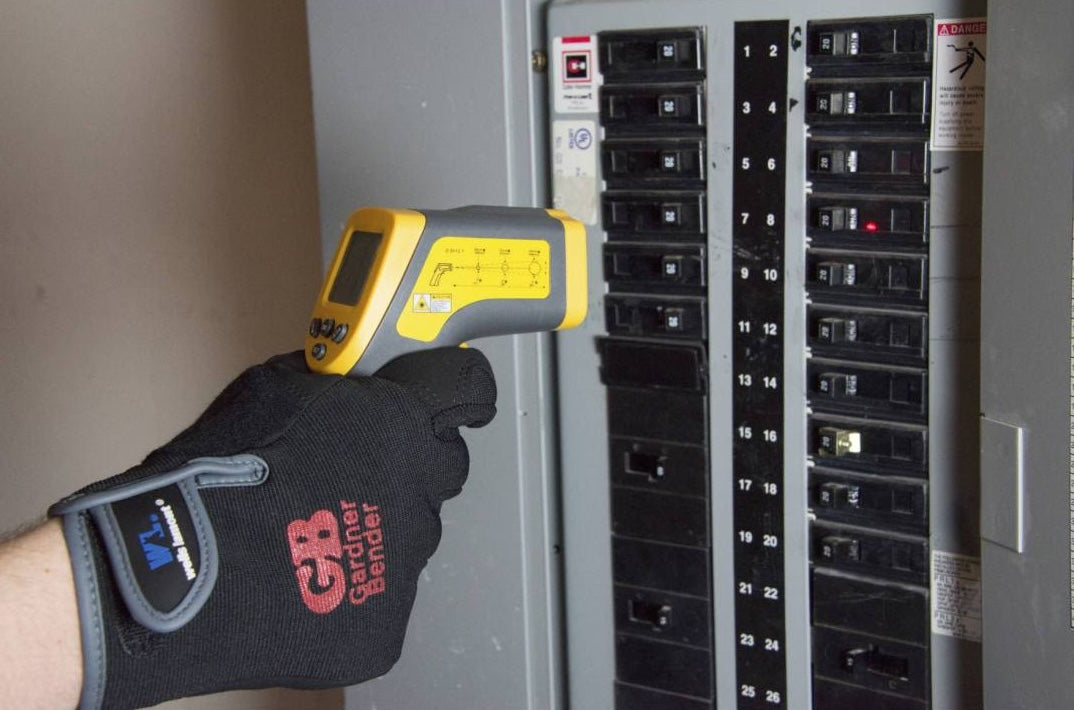 Person wearing Gardner Bender glove using yellow and gray infrared thermometer on home electrical panel for temperature check