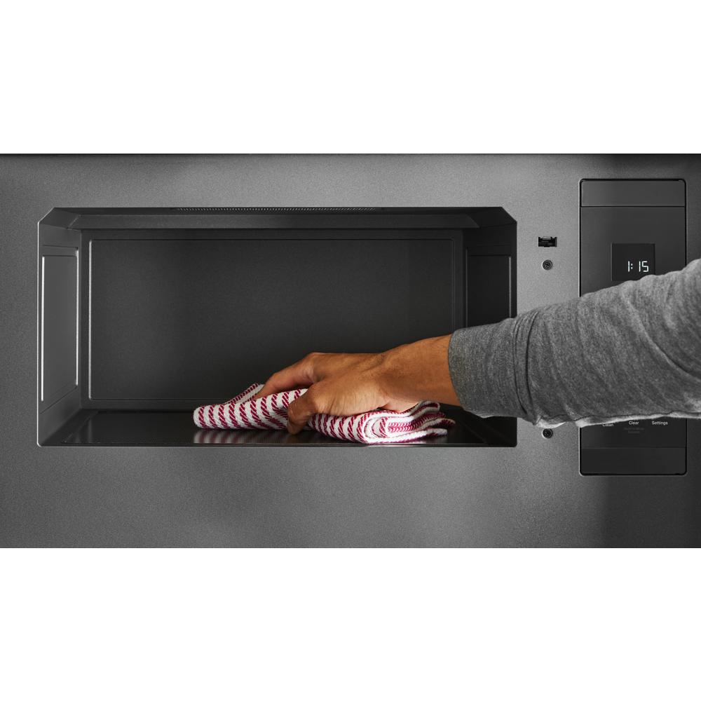 Hand cleaning interior of black over-the-range microwave with digital control panel in modern kitchen setting