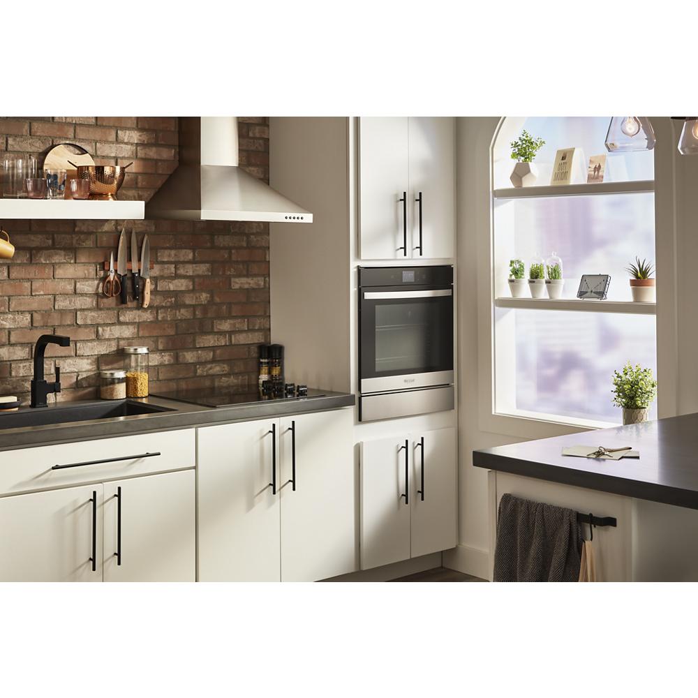 Built-in stainless steel convection wall oven installed in kitchen with white cabinetry and brick backsplash wall