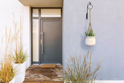 Black steel curved planter hanger mounted on exterior wall holding a white pot with greenery near modern front door