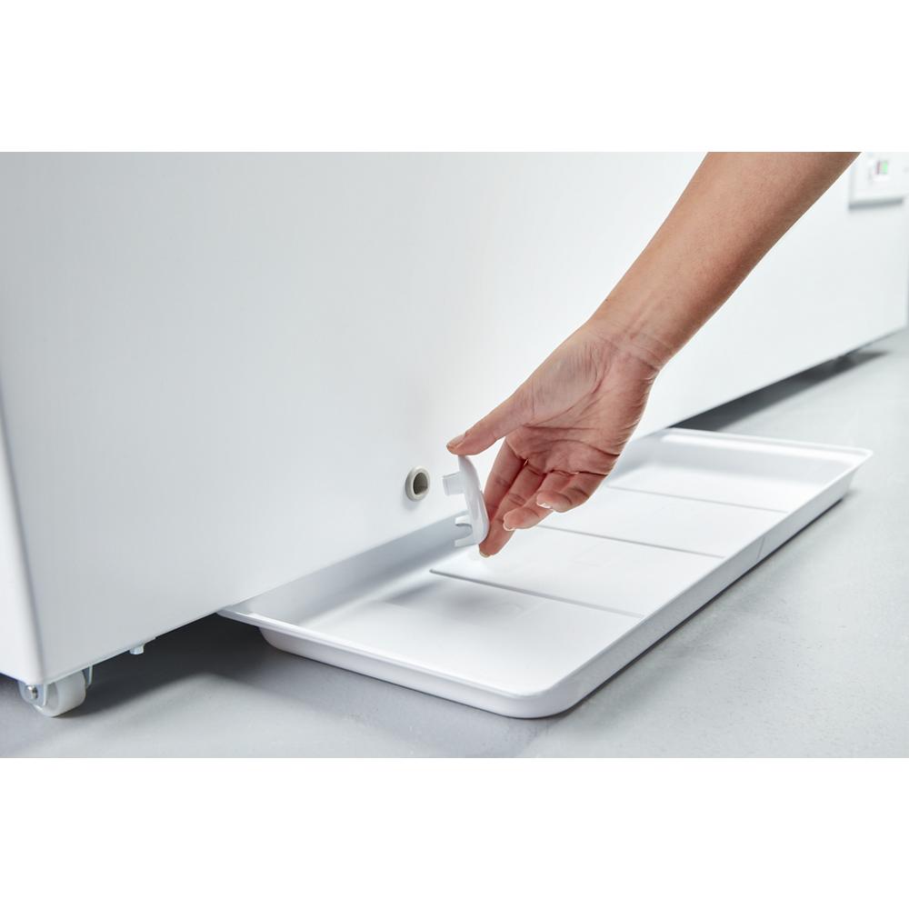 Hand removing drip tray from drain hole at base of white chest freezer in kitchen appliance setting from Freezers collection