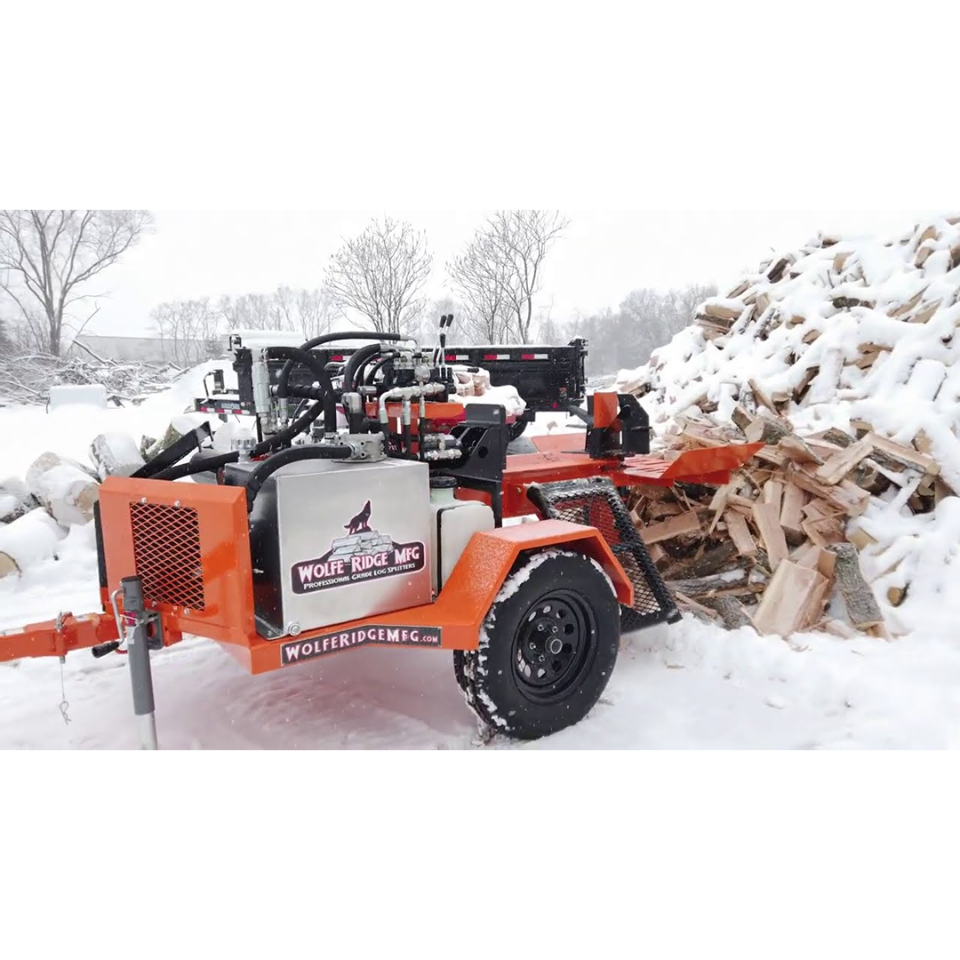 Orange Wolfe Ridge commercial log splitter trailer with hydraulic controls near large snow-covered firewood pile outdoors