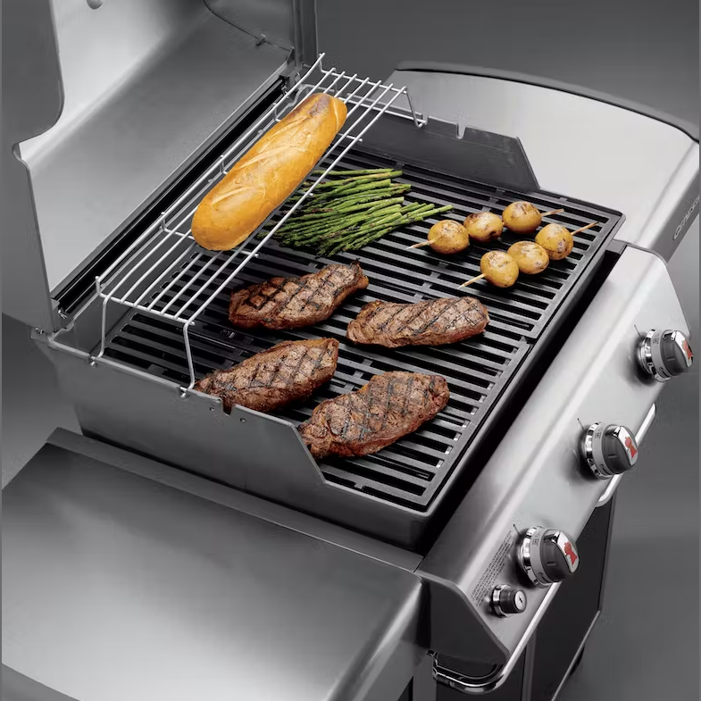 Porcelain-enameled cast iron cooking grates on grill with steaks, asparagus, potatoes, and warming rack with bread loaf in outdoor living collection