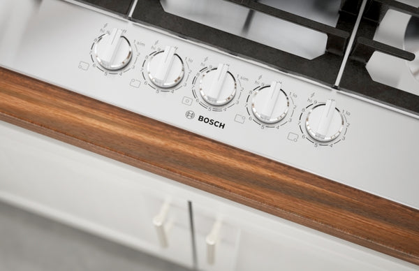 Close-up of stainless steel cooktop control panel with five knobs and wood trim for kitchen and home improvement use