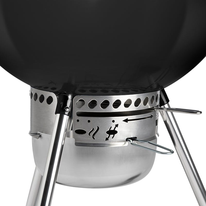 Close-up of adjustable air vent and ash catcher on a black charcoal grill for outdoor grilling enthusiasts.
