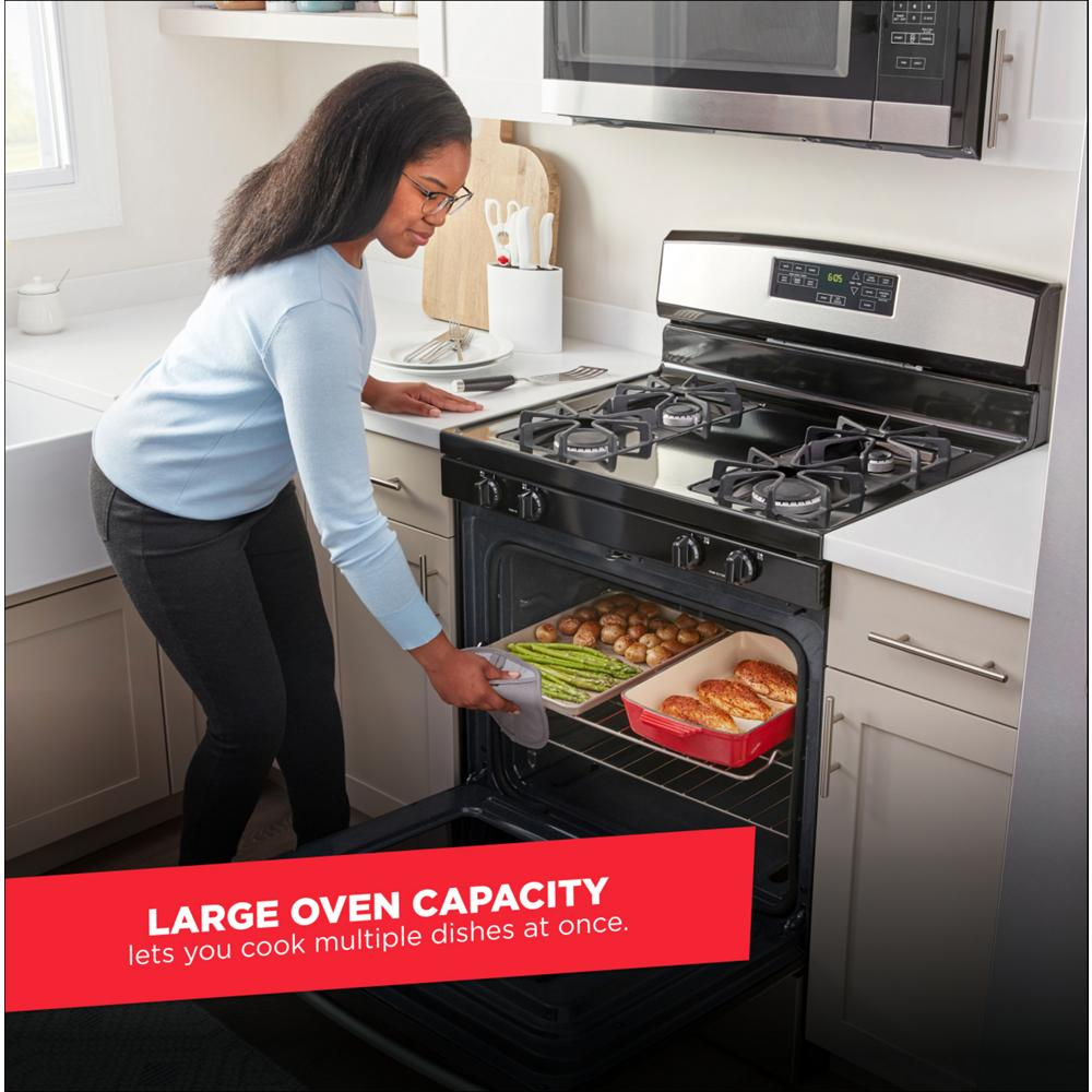 Woman removing baked chicken and vegetables from open oven on black gas range in modern kitchen setting