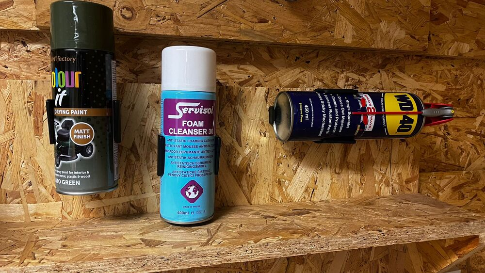 Three aerosol cans secured in black StealthMounts holders on a wooden garage storage panel for tool organization