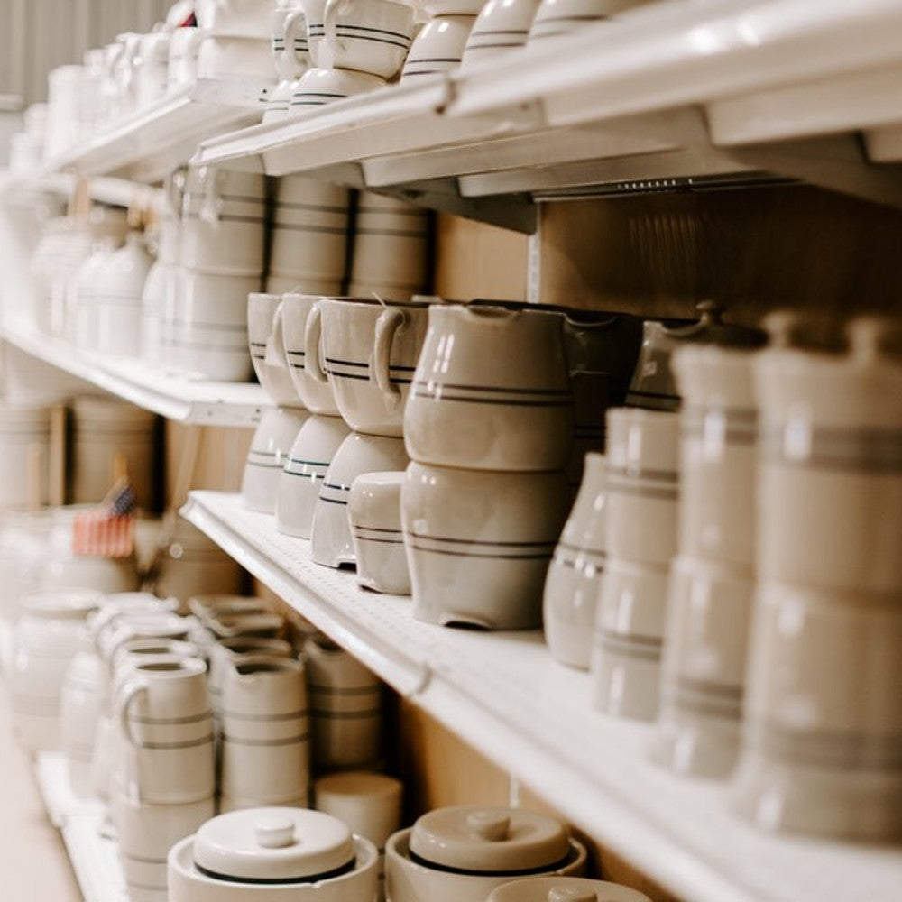 Shelves lined with cream-colored stoneware featuring subtle blue stripes, part of a kitchenware and serveware collection under $50