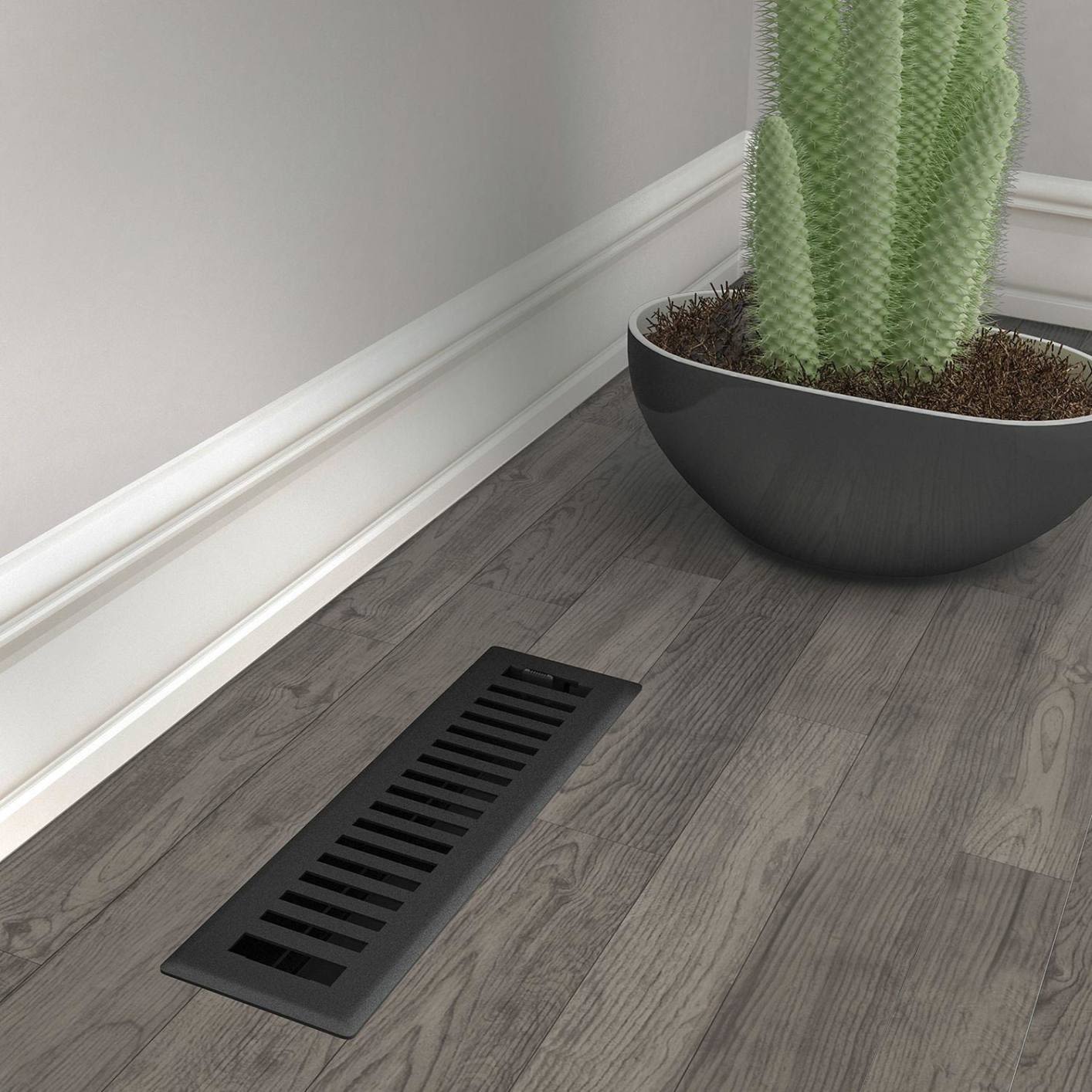 Black iron floor register with adjustable vents installed on wood flooring near wall and potted cactus plant
