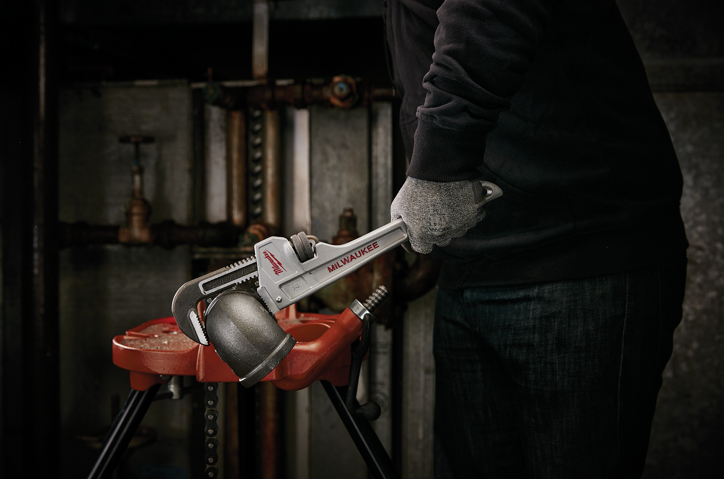 Person using a Milwaukee aluminum pipe wrench to tighten plumbing fitting on a red pipe vise for home improvement tasks