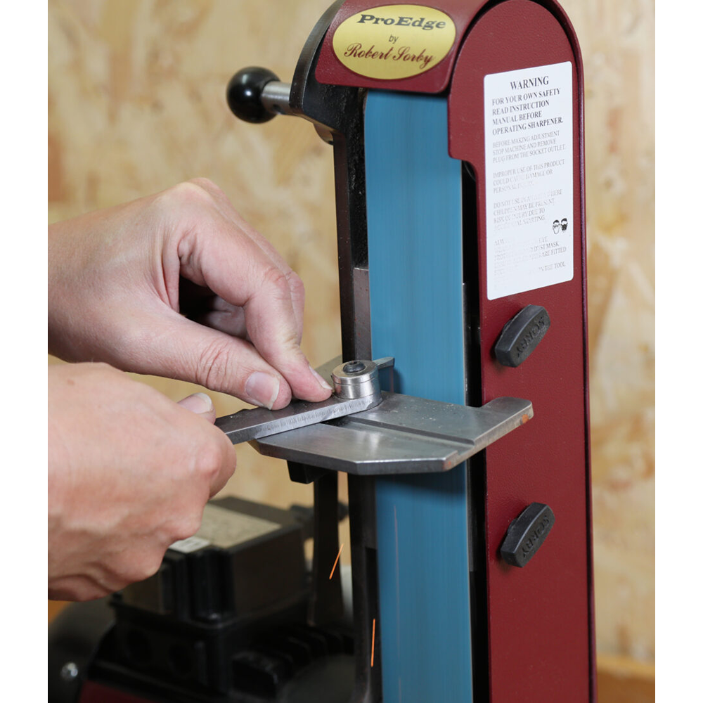 Hands sharpening a metal cutting tip holder on a vertical belt sander for precise tool maintenance and home improvement tasks