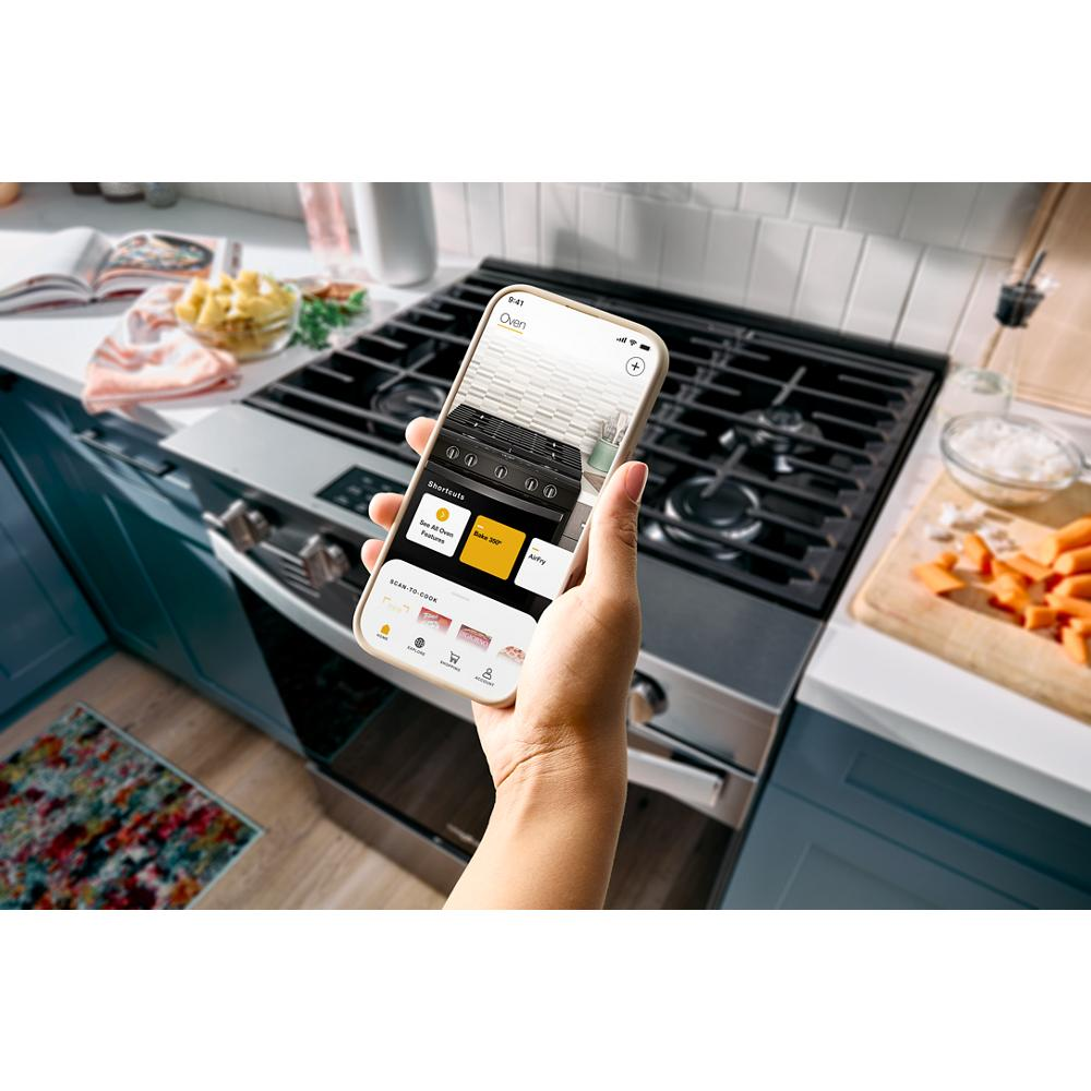 Person holding smartphone with smart range app open over a stainless steel gas range in a modern kitchen setting