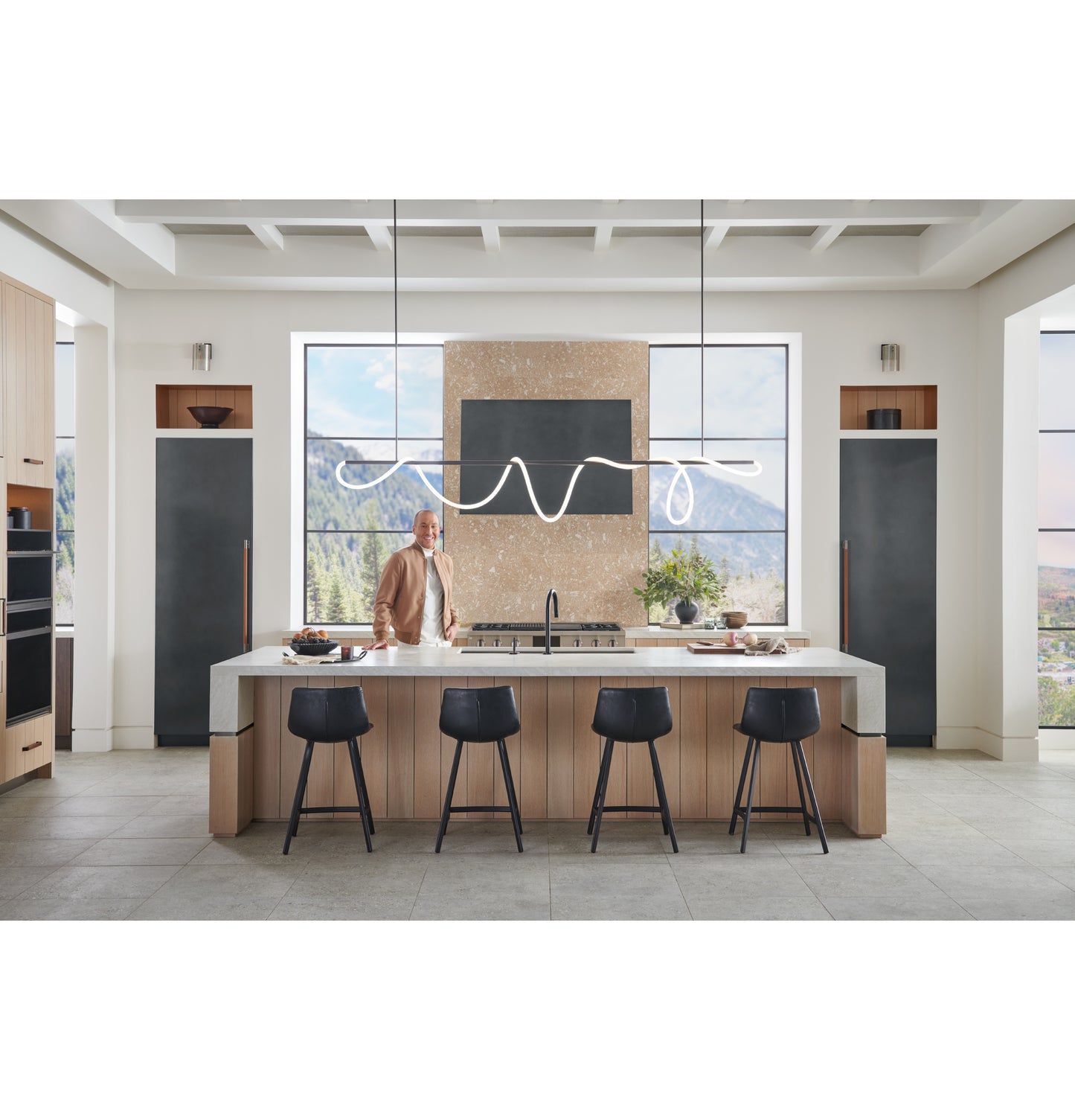 Spacious modern kitchen with a large island, black stools, designer range hood, and scenic mountain views in appliances collection