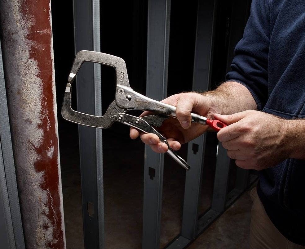 Close-up of hands using locking C-clamp with regular jaws on metal pipe in woodworking and home improvement setting