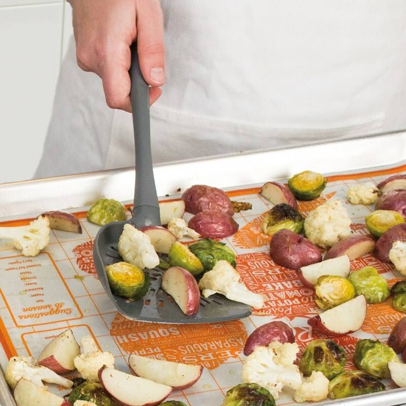 Charcoal wide-headed turner lifting roasted vegetables on a baking sheet for kitchen utensil use