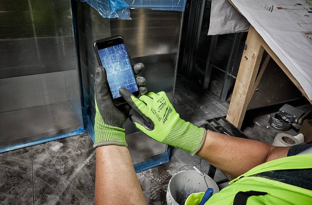 Worker wearing large hi-vis green gloves with black polyurethane palms using touchscreen smartphone on job site