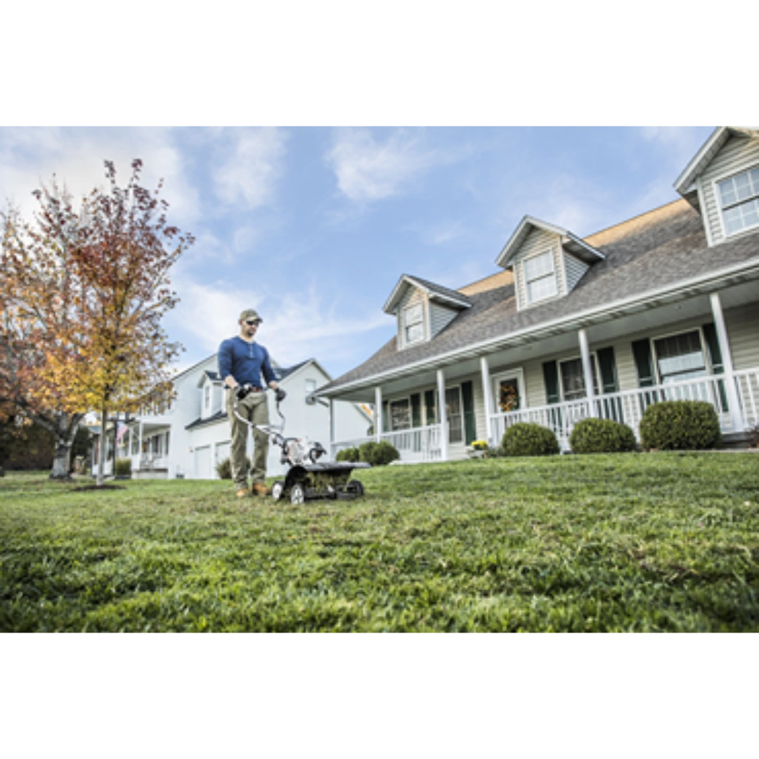 Person operating a gas-powered yard tiller with wheel kit on a suburban lawn for home improvement tasks
