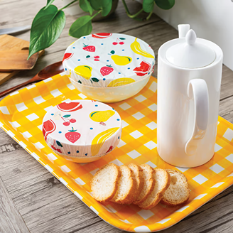 Set of reusable bowl covers with bright fruit and vegetable prints on yellow checkered tray in kitchen storage collection