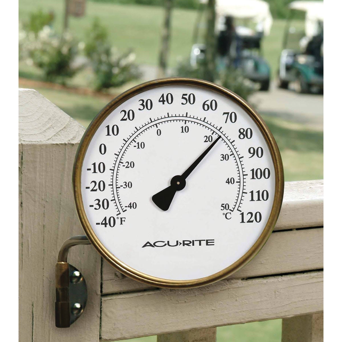 Round metal outdoor thermometer mounted on wood fence with temperature displayed in Fahrenheit and Celsius