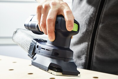 Person holding a cordless orbital sander with dust extraction attachment while sanding wood for home improvement tasks