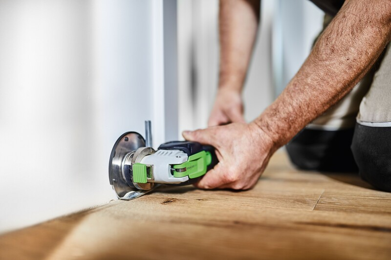 Cordless oscillating tool with ergonomic grip cutting into wooden floor during home improvement project
