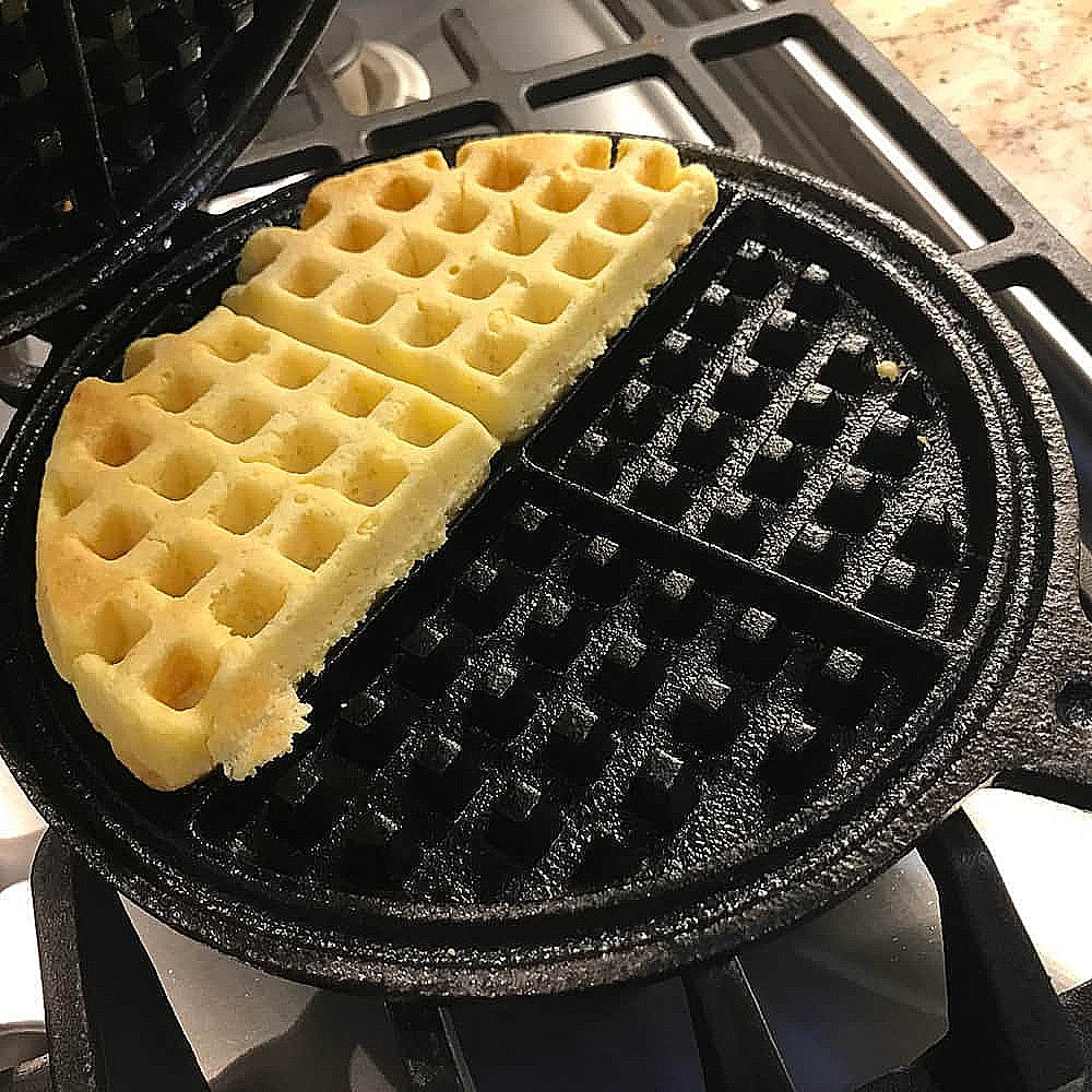 Half-cooked waffle batter inside a black cast iron stovetop waffle maker on a gas stove burner in kitchenware setting