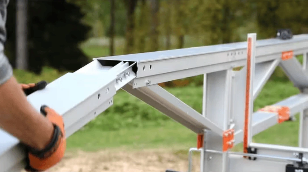 Close-up of a person adjusting a metal extension frame with orange connectors for woodworking or home improvement tasks