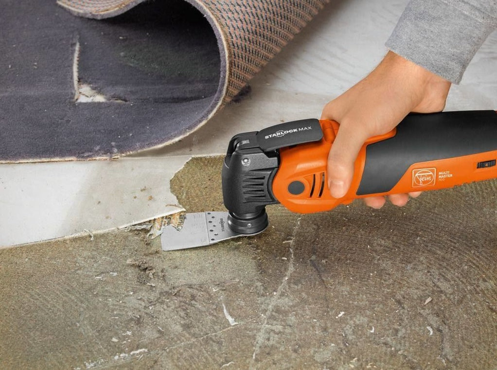 Orange and black oscillating multitool removing carpet adhesive for home improvement and remodeling tasks