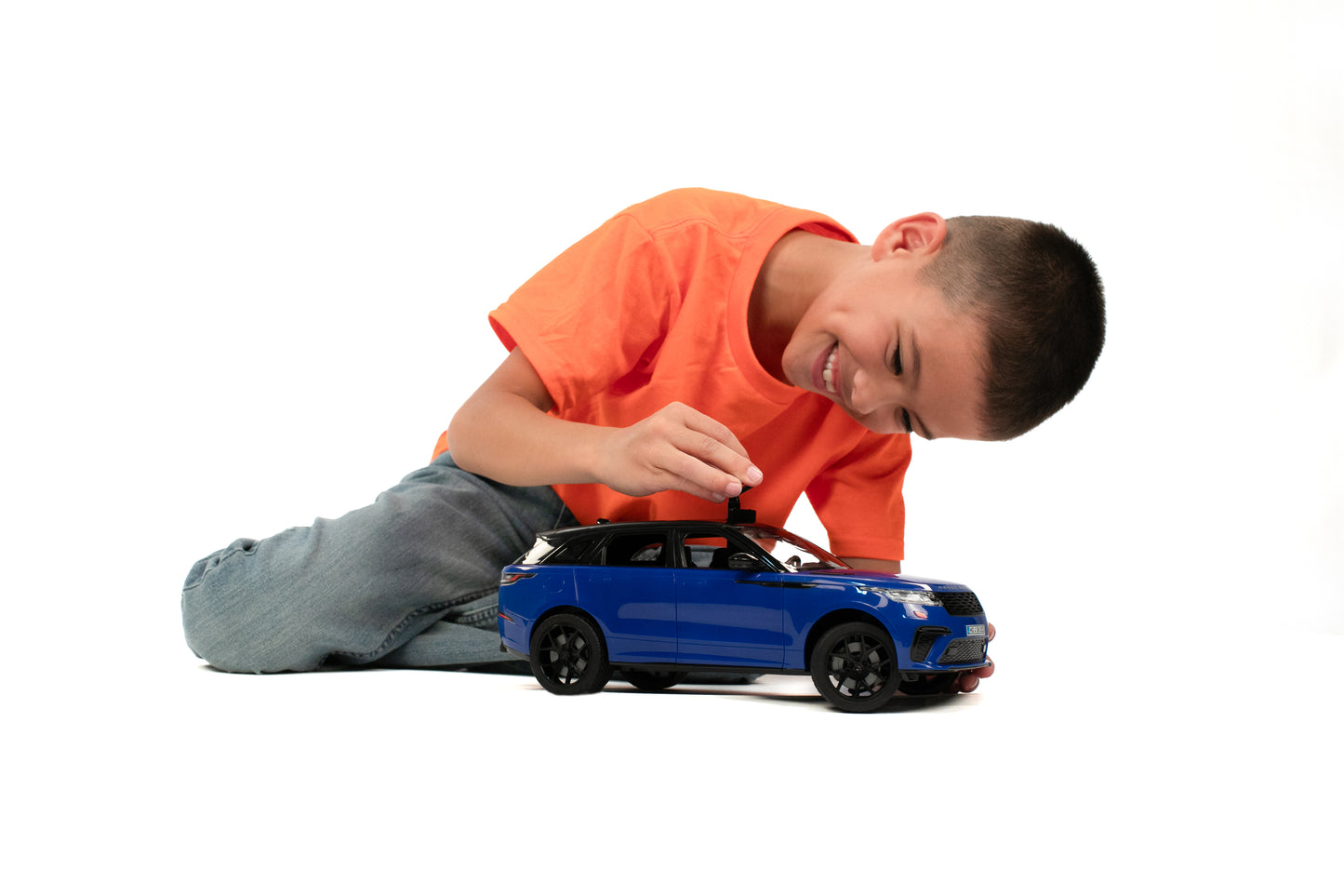 Boy smiling while playing with detailed blue Bruder Range Rover Velar toy car on white background