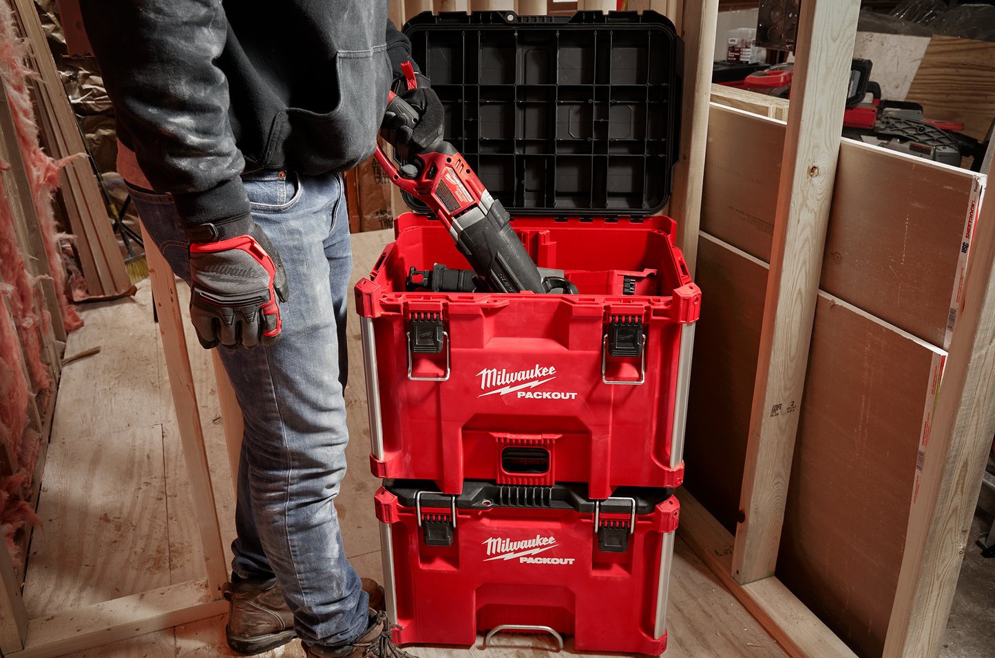 Stacked red Milwaukee PACKOUT XL tool boxes in a workshop with a person storing a power tool inside, showing jobsite storage use