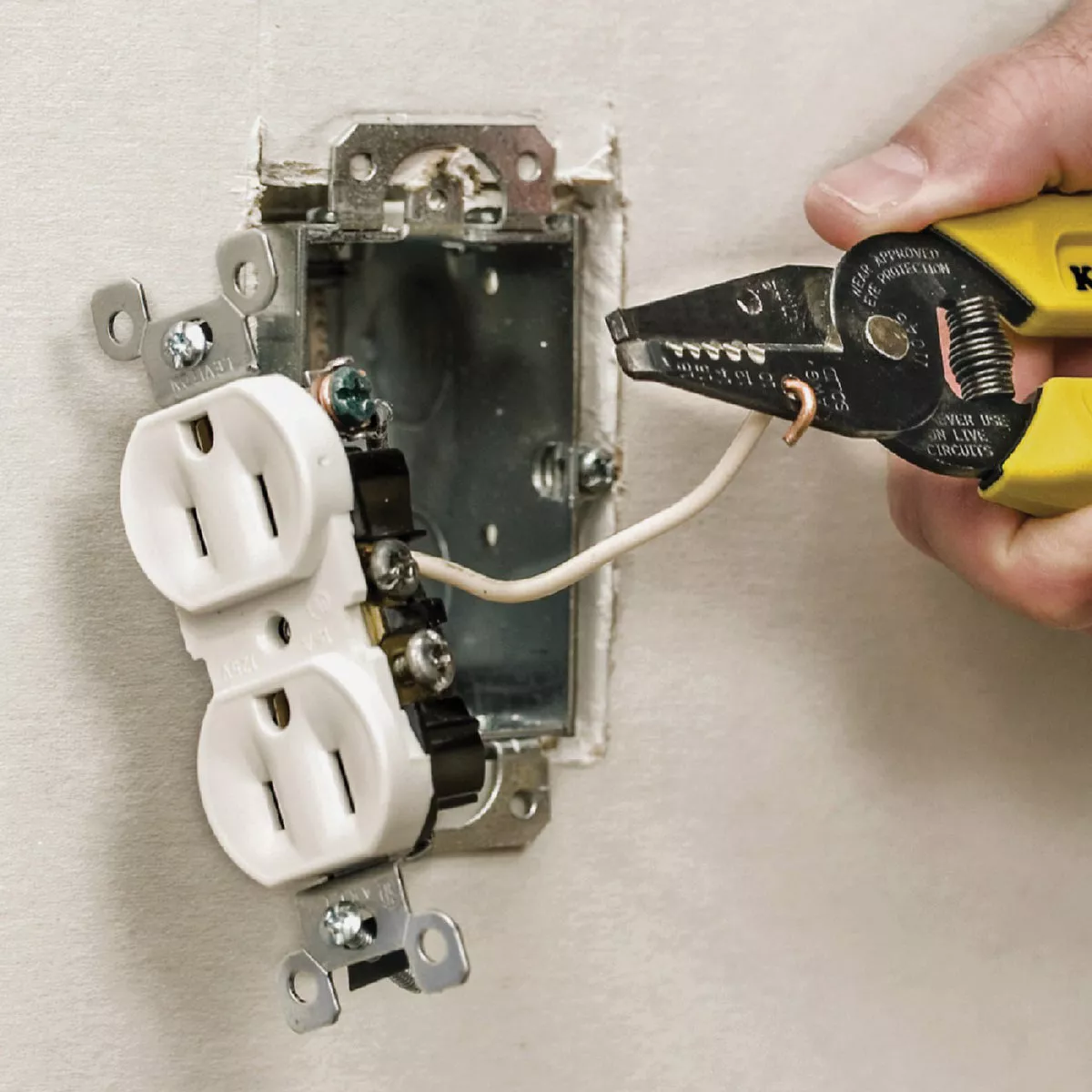 Yellow-handled wire stripper gripping white solid electrical wire near a wall outlet for home improvement tasks
