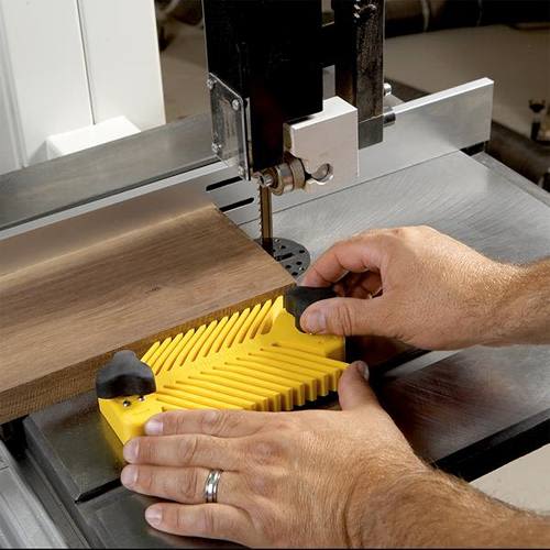 Close-up of hands positioning a yellow Magswitch Universal Featherboard on a woodworking bandsaw for tool accessory use