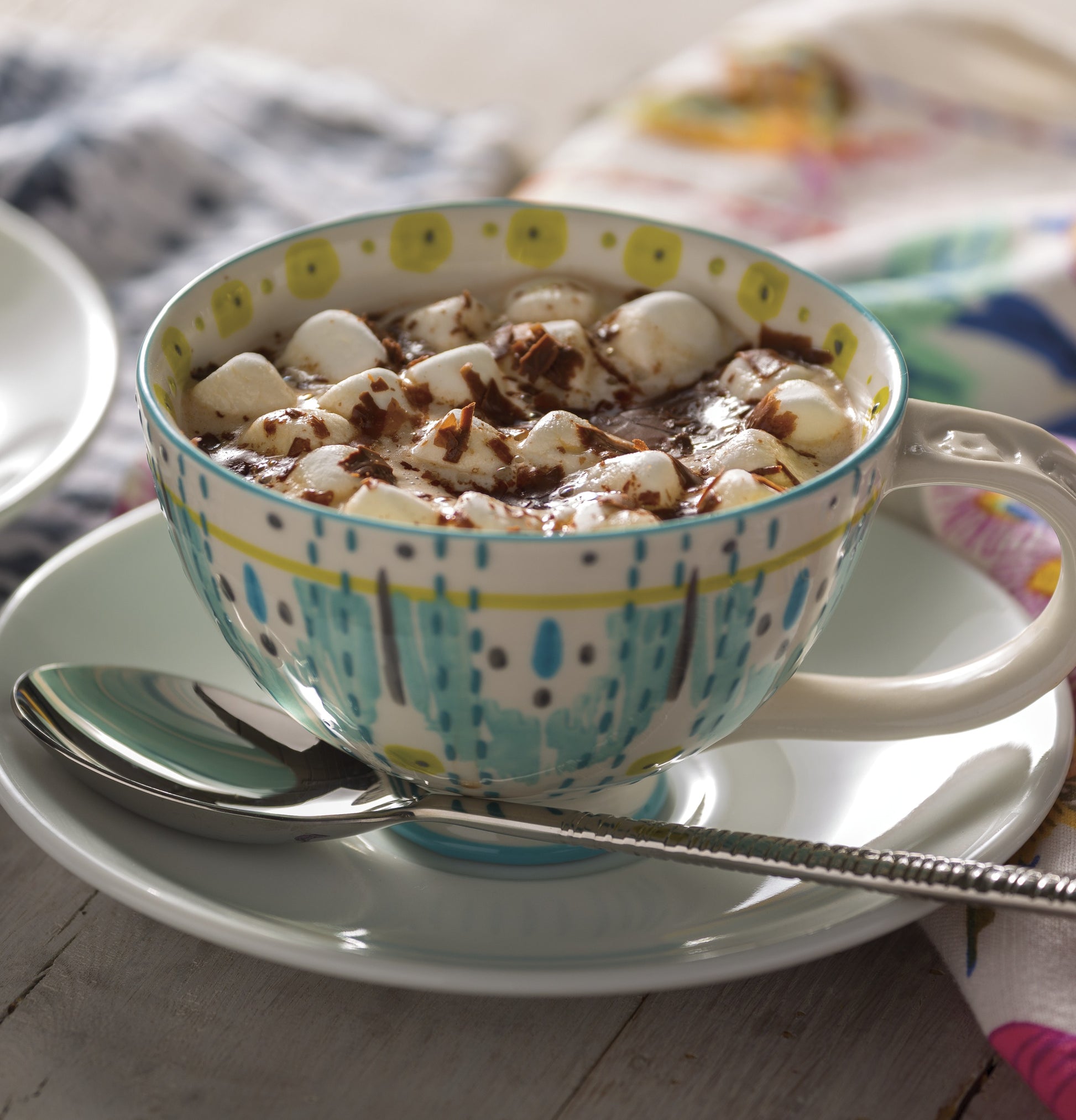 Decorative ceramic cup filled with hot chocolate topped with marshmallows and chocolate shavings on a saucer with spoon
