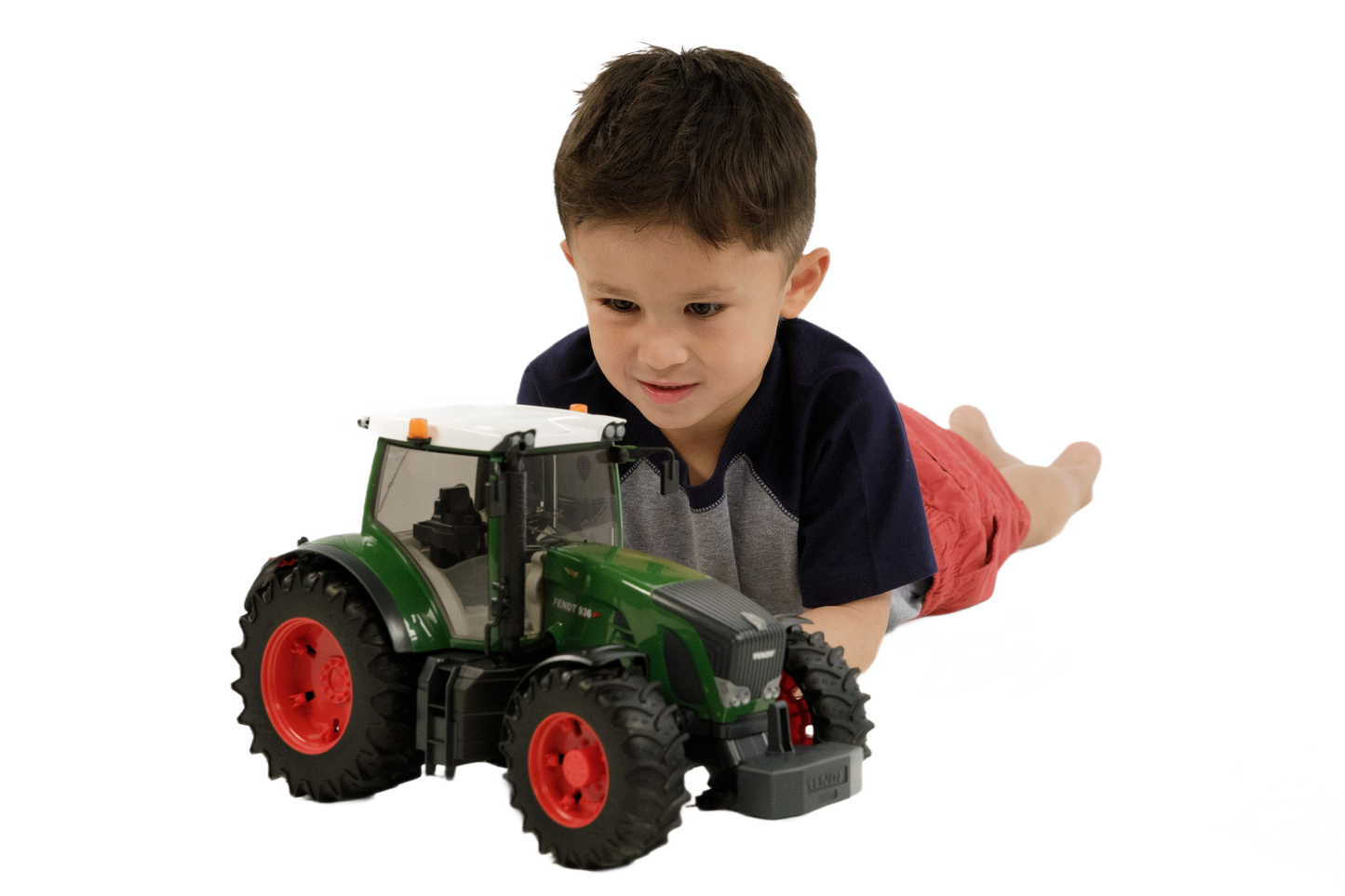 Young boy lying on floor playing with green Bruder Fendt 936 Vario Tractor toy featuring detailed cabin and red wheels