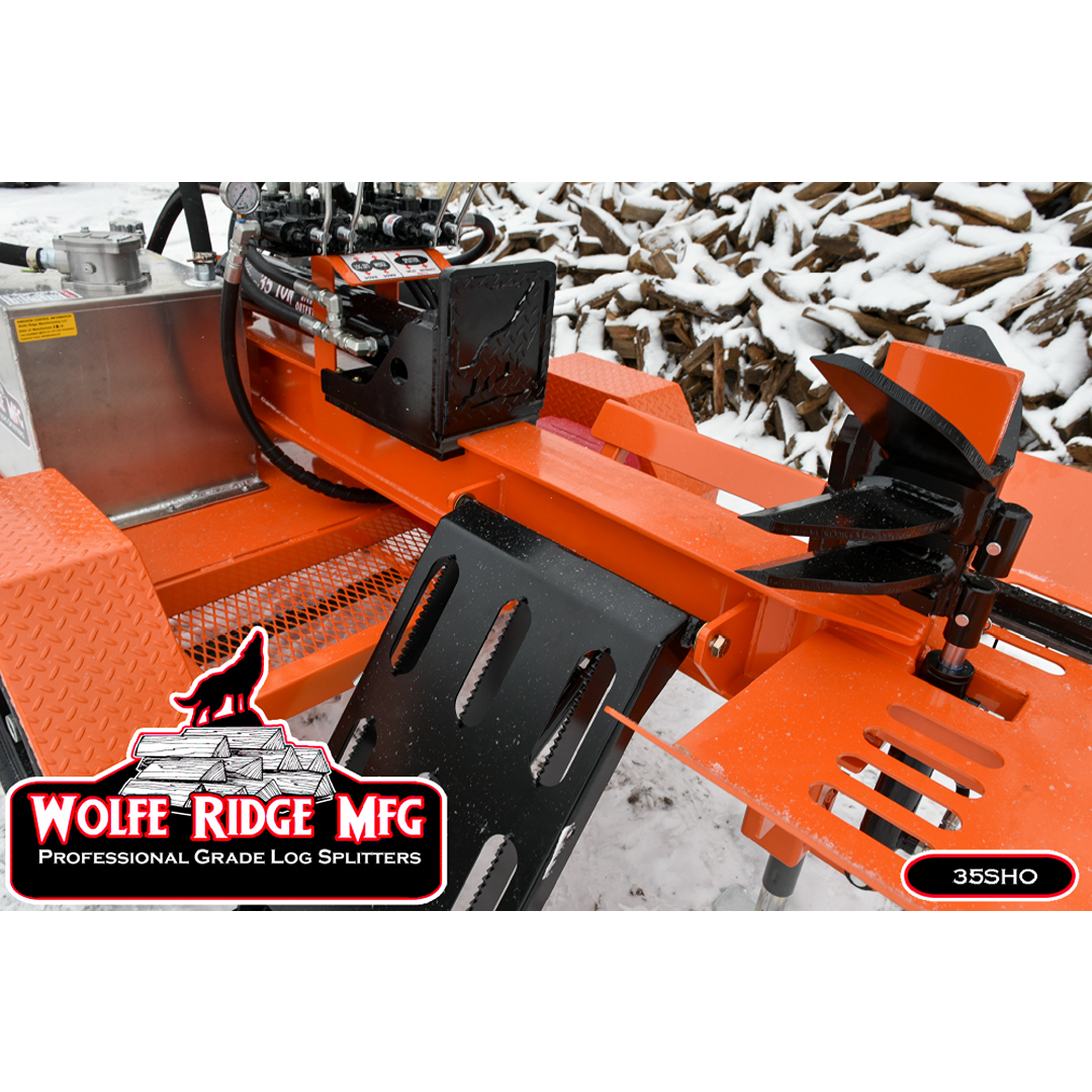 Orange commercial log splitter with hydraulic controls and metal log cradle on snowy ground near stacked firewood outdoors