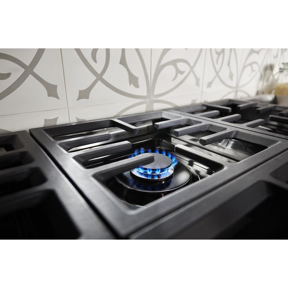 Close-up of blue gas burner flame on black cast iron grate of KitchenAid stainless steel dual fuel range from Ranges collection.