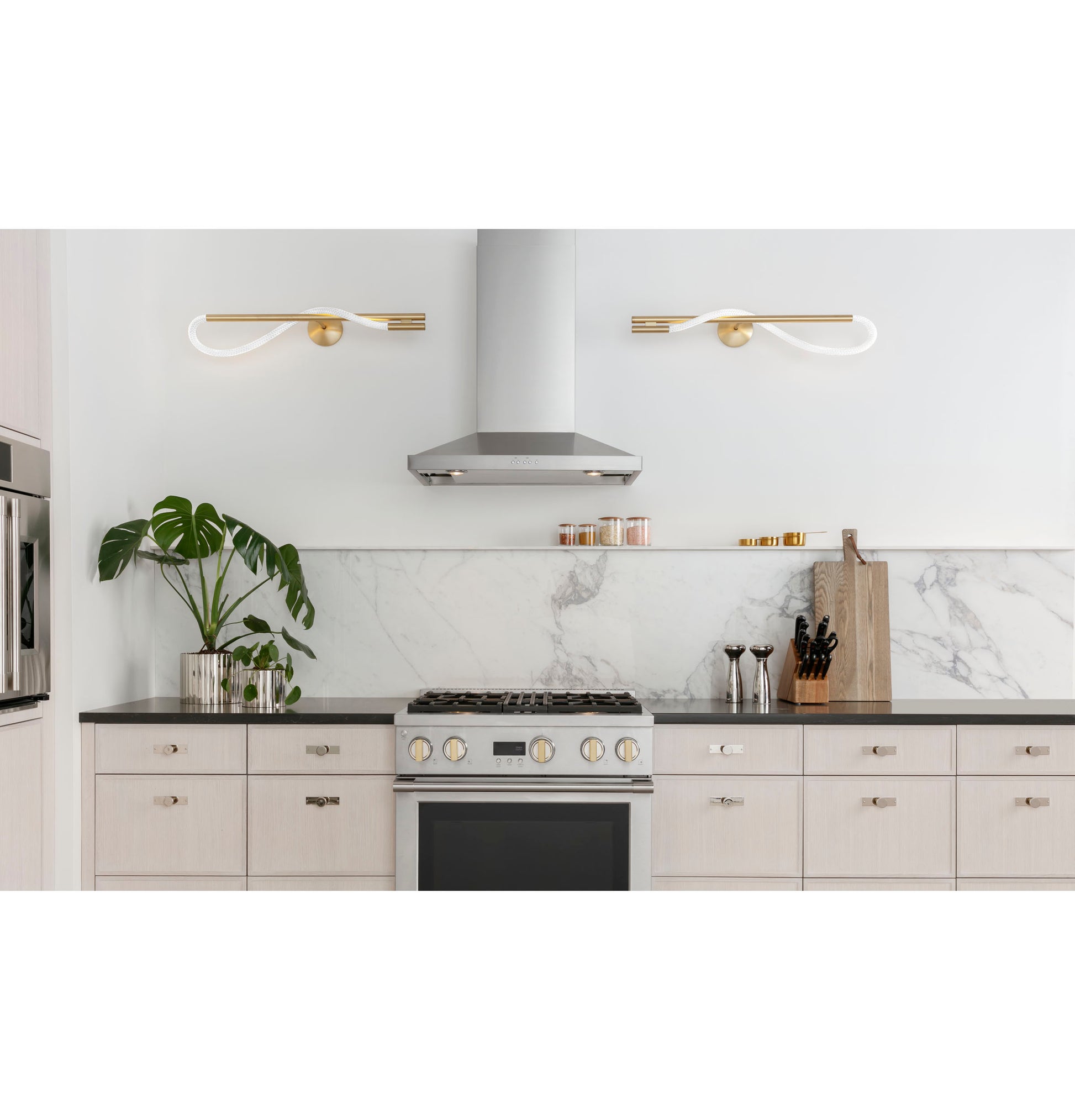 Stainless steel wall-mounted vent hood centered above gas cooktop with modern cabinetry and marble backsplash in kitchen setting