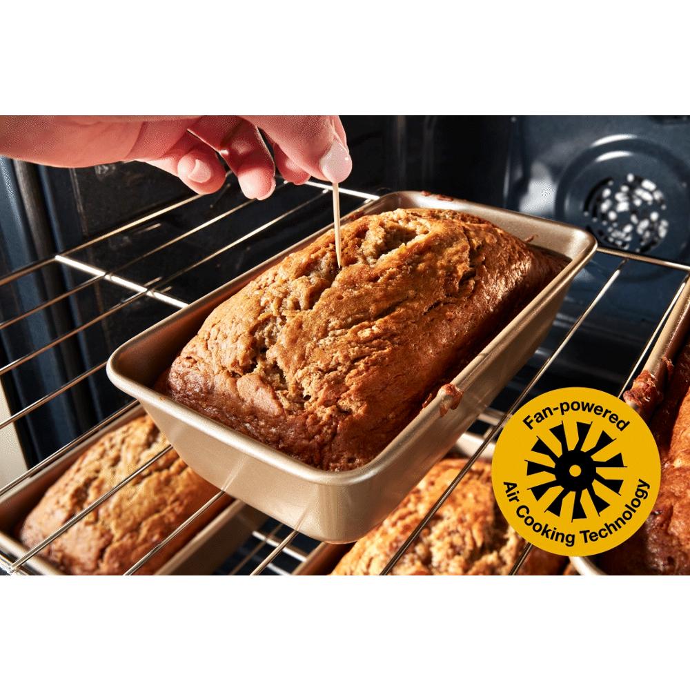 Hand testing a golden brown loaf in a metal pan inside a gas range oven with fan-powered air cooking technology