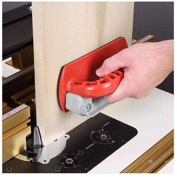 Hand holding red and gray push block with integrated hand guard on woodworking table under $100 tools collection