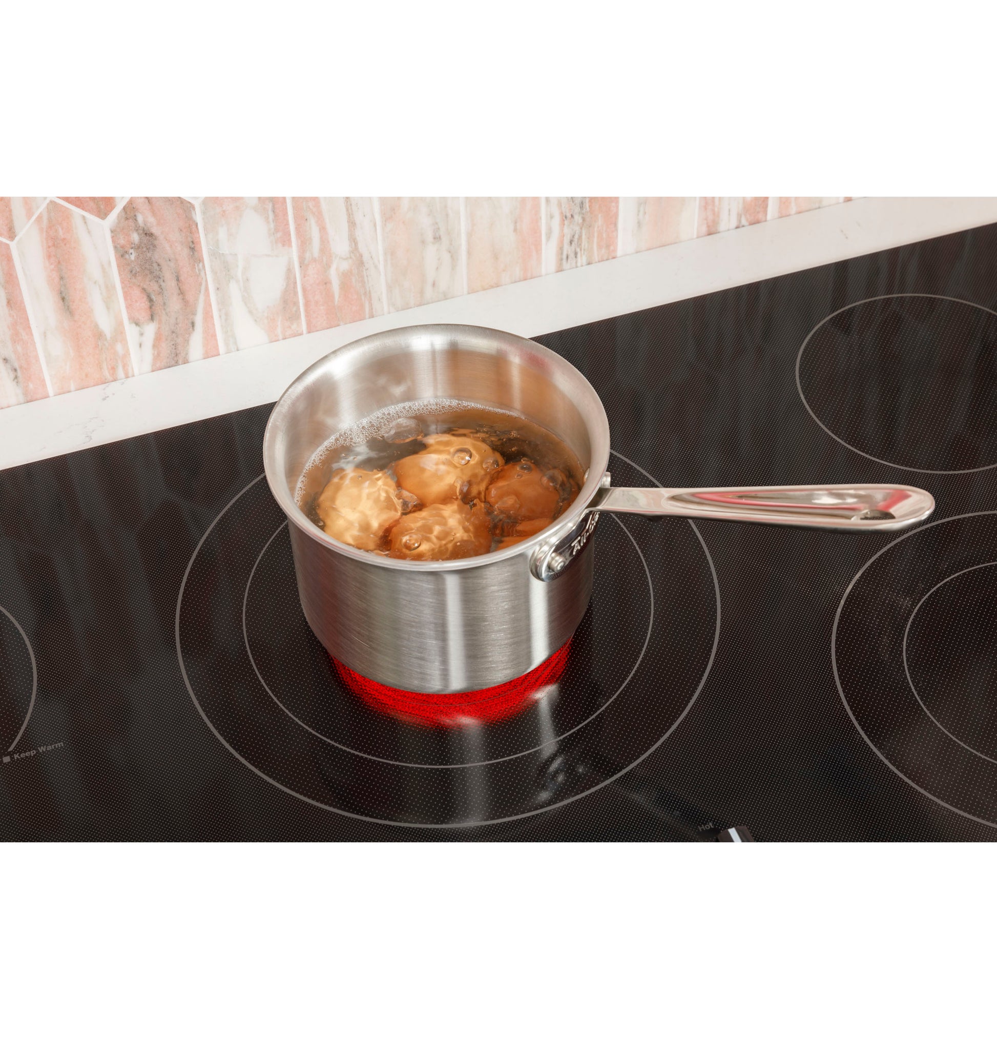 Stainless steel pot boiling potatoes on red glowing burner of a black built-in knob control electric cooktop