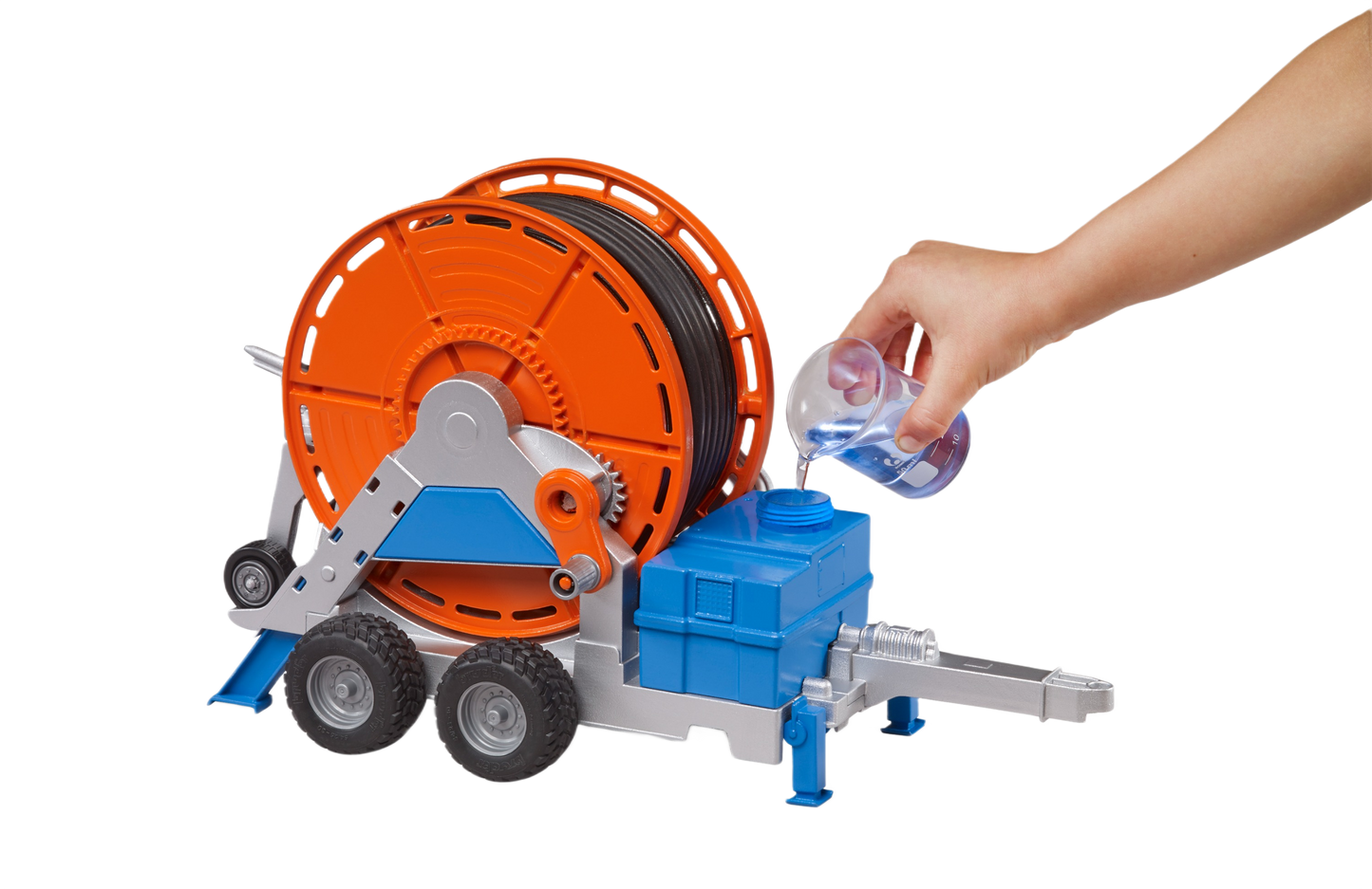 Toy irrigation trailer with orange hose reel and blue-gray base, shown with hand pouring water, in Bruder Toys collection