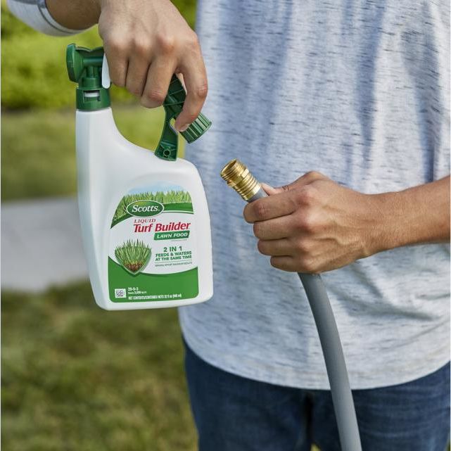 Person connecting garden hose to a white and green Scotts liquid lawn fertilizer spray bottle for lawn care tasks